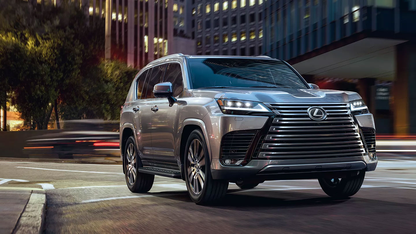 Silver Lexus SUV on a city street at dusk, with blurred traffic lights in the background.