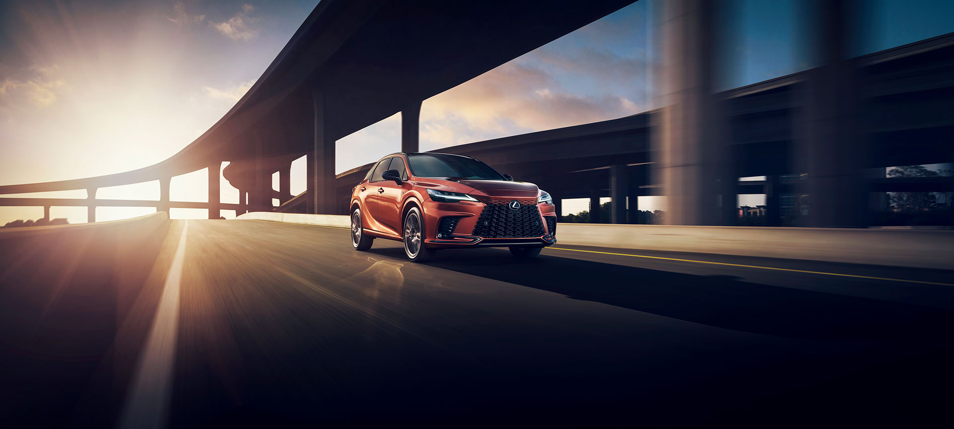 A sleek red Lexus SUV navigating a curve on an urban highway during sunset.